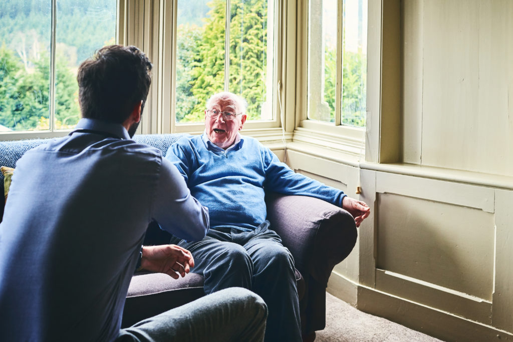 Older man talking with younger man in brightly lit nursing home to represent a pastoral visit