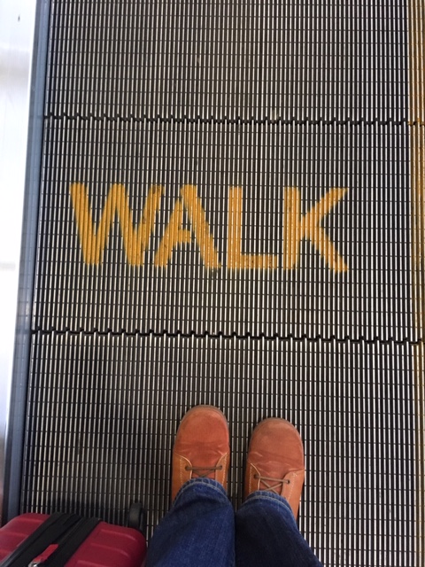 The word "WALK" on a moving walkway, with a pair of brown shoes standing