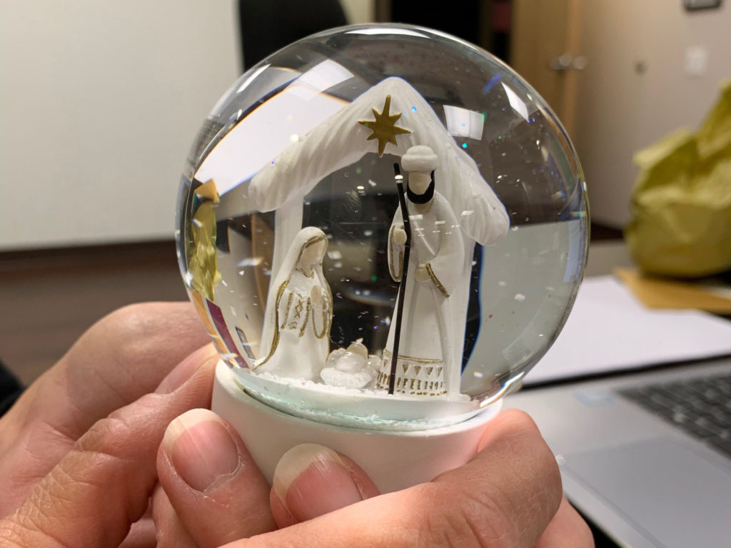 Two hands hold a snow globe with Mary, Joseph, and Jesus inside