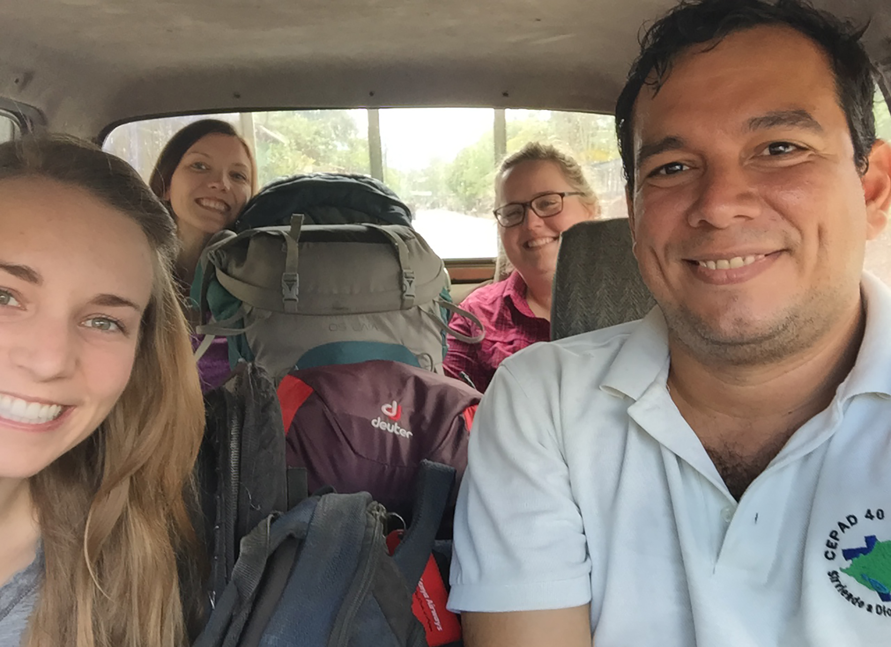 Three smiling young white American women are crammed into a van with a Nicaraguan man and lots of luggage