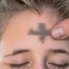 A thumb sweeps a horizontal stroke of ash on a young boy’s forehead, completing the sign of the cross.