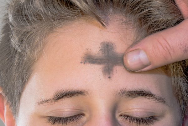 A thumb sweeps a horizontal stroke of ash on a young boy’s forehead, completing the sign of the cross.