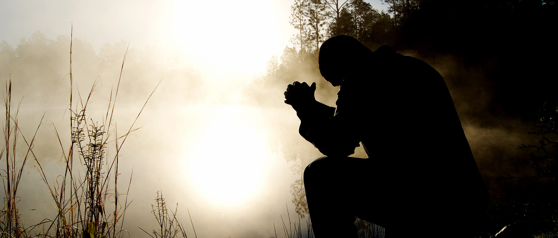 Silhouette of a man with elbows on his knees and hands folded in prayer