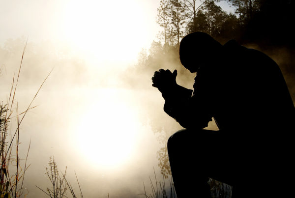 Silhouette of a man with elbows on his knees and hands folded in prayer