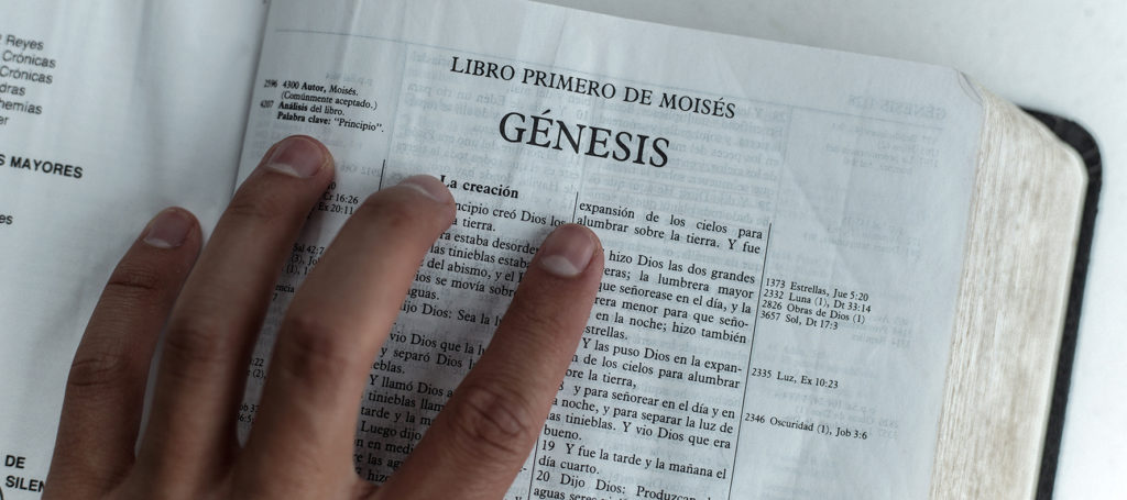 La mano en la Biblia que está abierta en el Génesis 1
