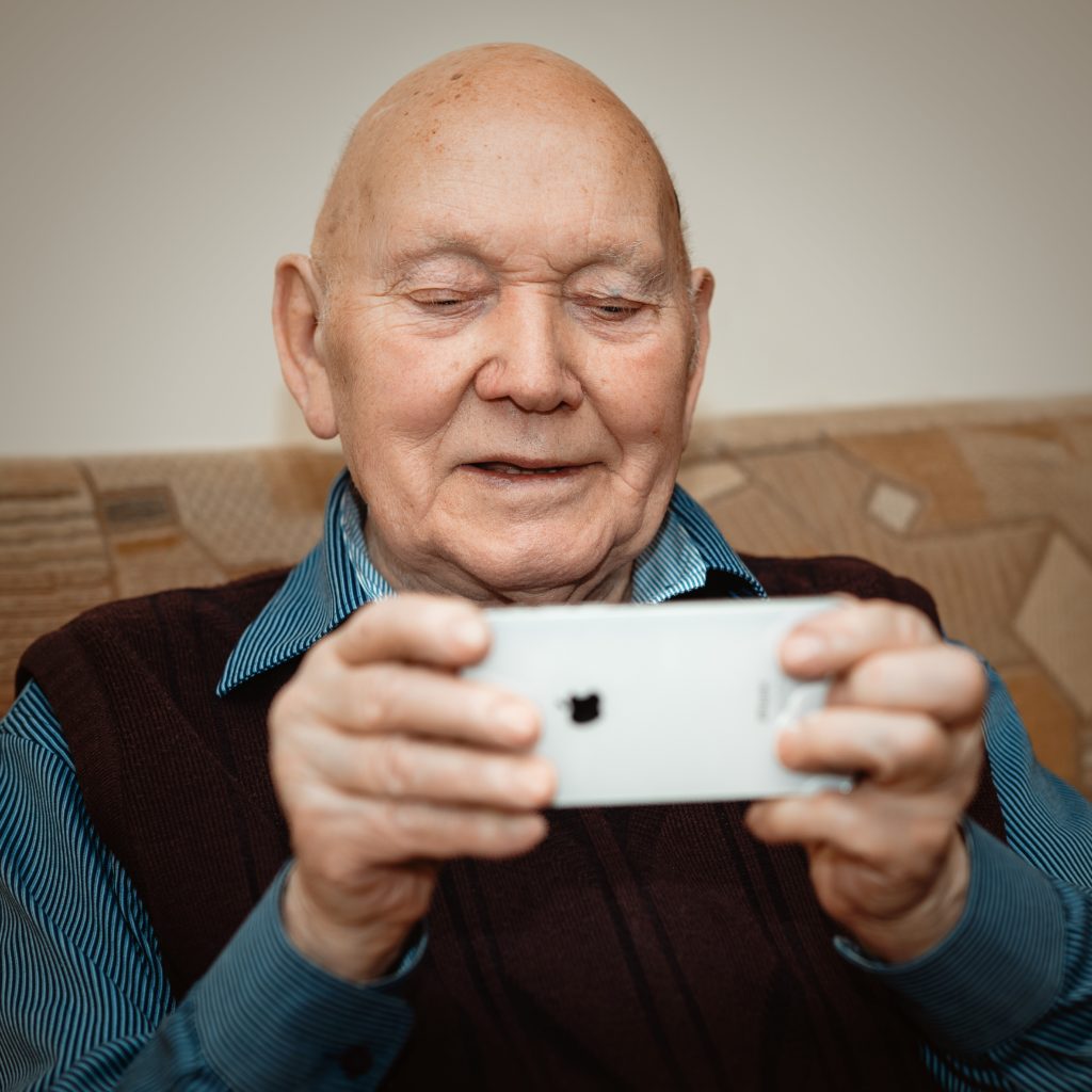 Older man using an iPhone to FaceTime, as many of us are dong now to stay connected during the coronavirus pandemic