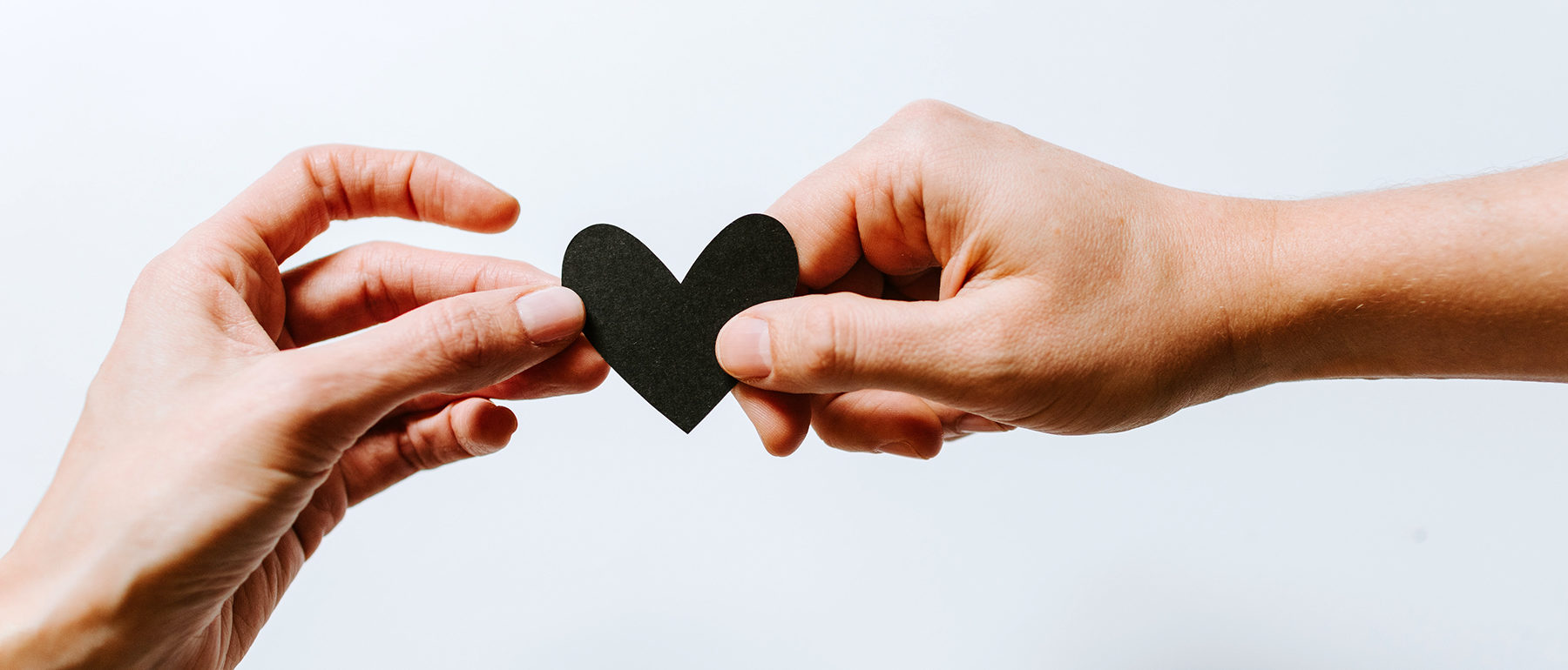 Two hands holding one small black heart between them