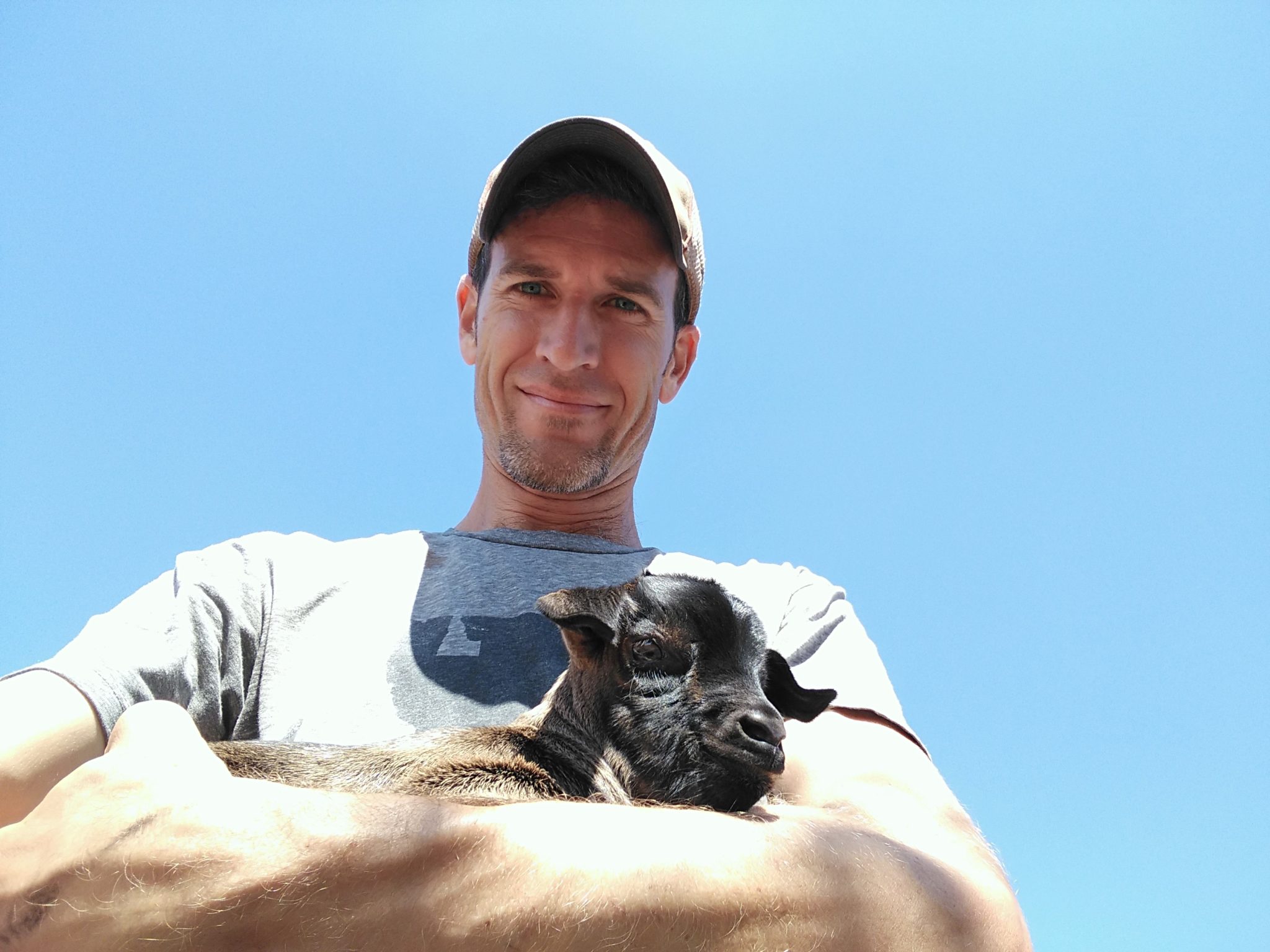 Caucasian man with cap hold a young goat in his arms