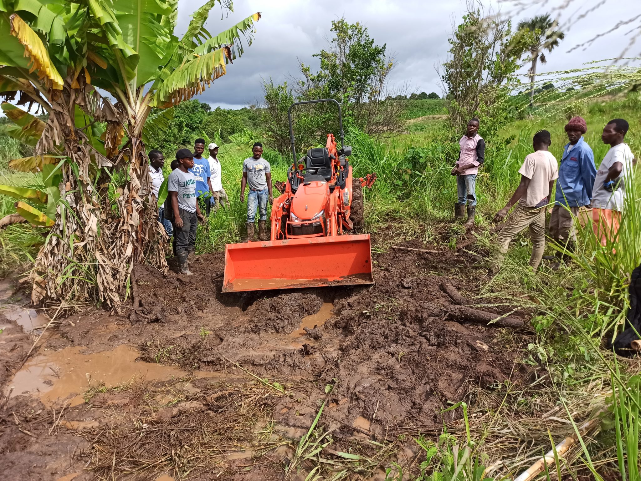 A handful of Mozambican farmers evaluate an orange tractor stuck in the mud