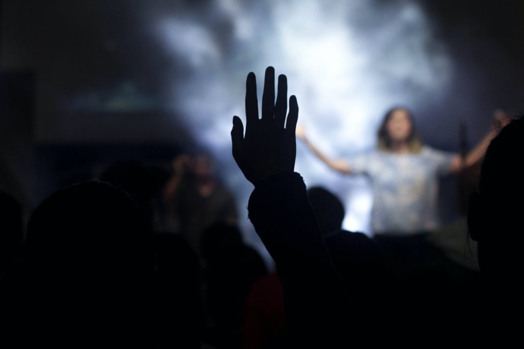 silueta de una persona con la mano derecha en el aire frente a una mujer en el escenario