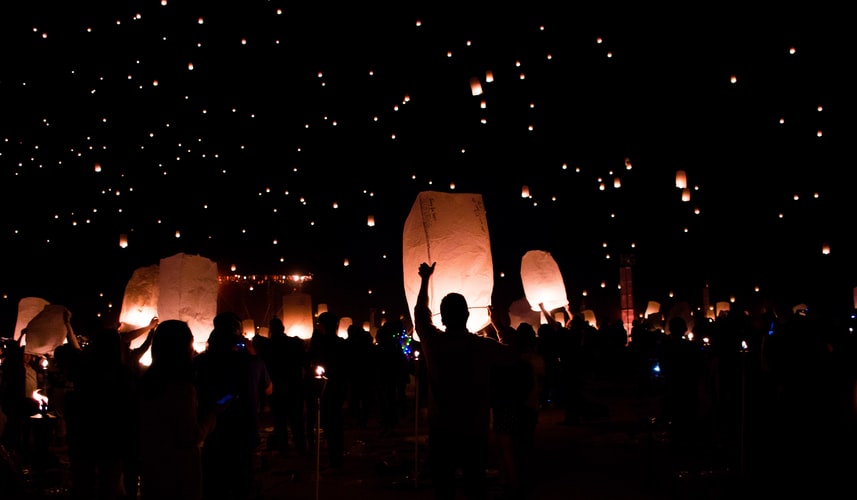 People lift glowing paper lanterns into the night sky.