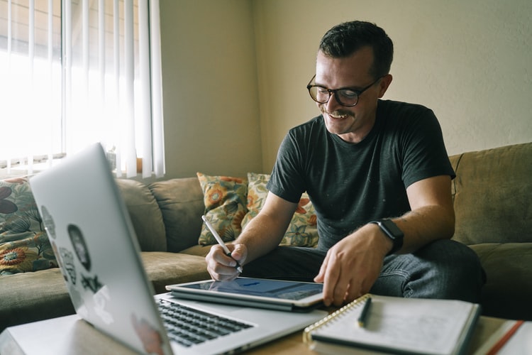 Un hombre sonríe mientras participa en un grupo en línea y toma notas.