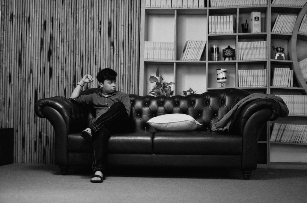 Black and white image of a young man sitting on one end of the couch in silence and solitude.