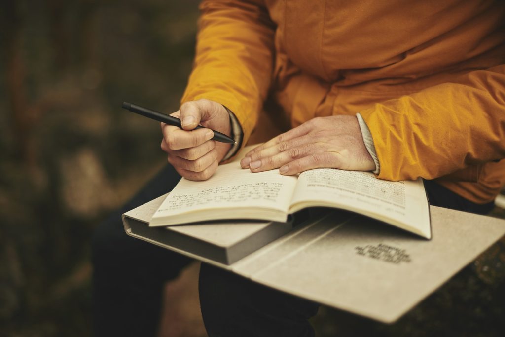 Cropped image of adult in yellow coat writing in a journal.