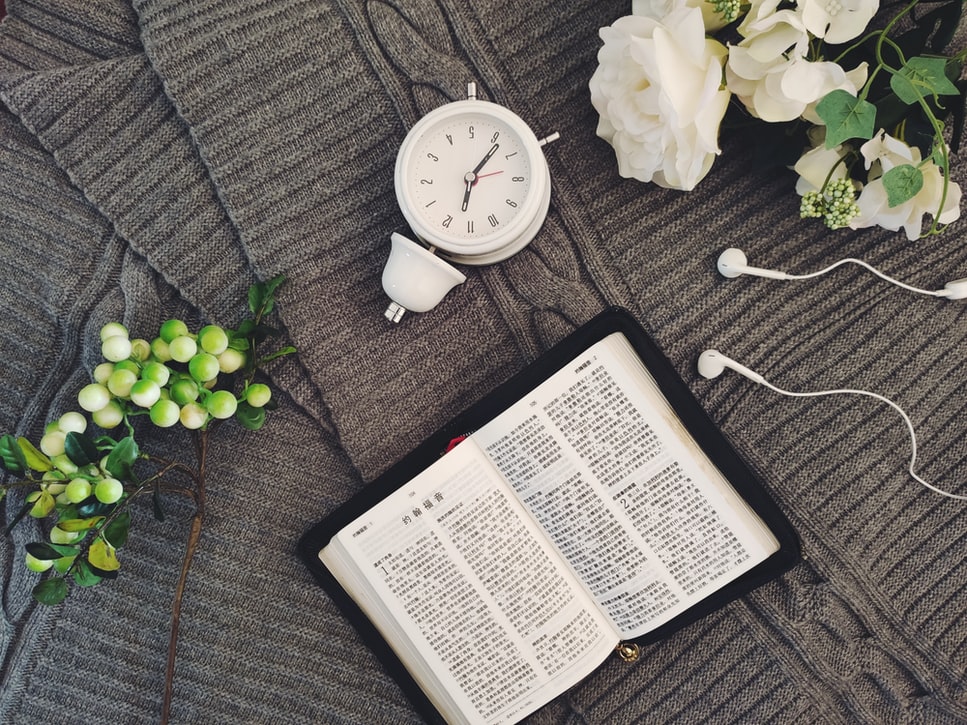 A clock and Chinese Bible lie on top of a gray knit blanket.