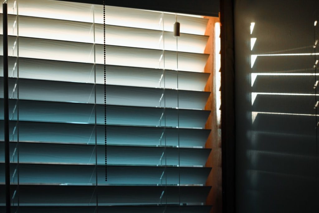 Sunlight through window blinds creates a blue and white gradation, with shadows on the wall.
