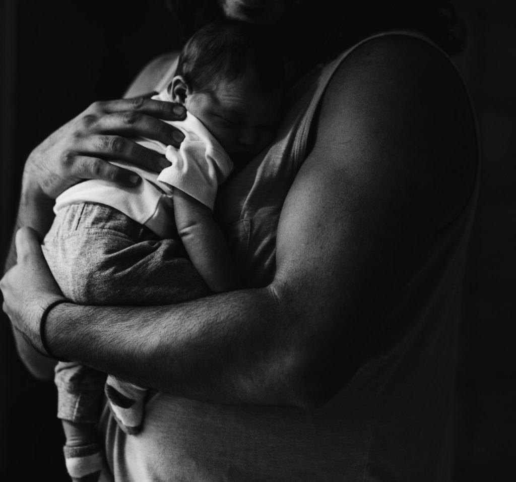 grayscale photography of man carrying a baby