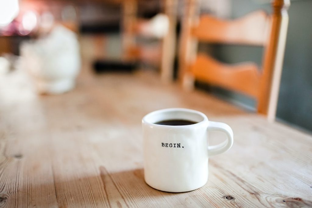 a white ceramic mug on a wooden table says "begin"