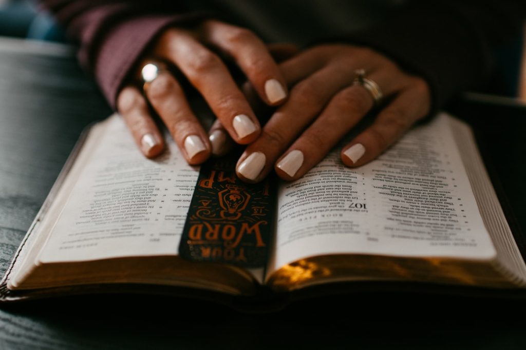 woman's hands are loosely folded over an open Bible with a bookmark