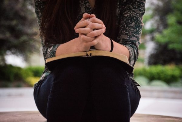 A young woman prays with her hands folded over an open Bible