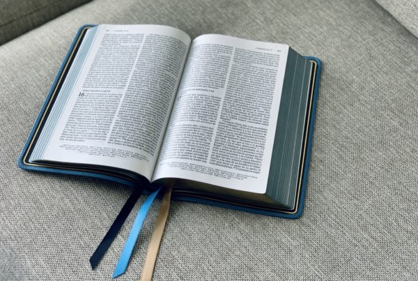 una Biblia encuadernada en cuero azul con marcadores de cinta multicolor está abierta en un sofá gris