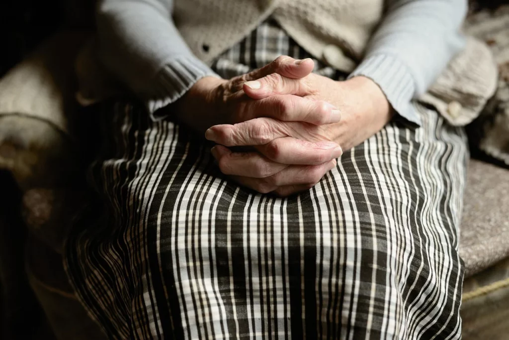 a woman's elderly hands are folded on top of her lap