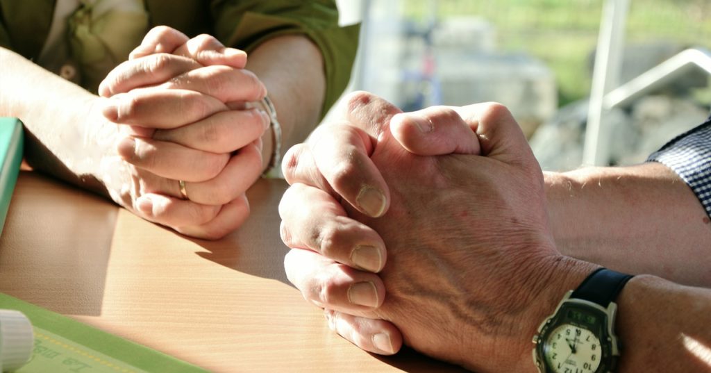 two sets of folded praying hands on a wooden table