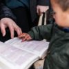 a young boy and his parent trace words on an open Bible