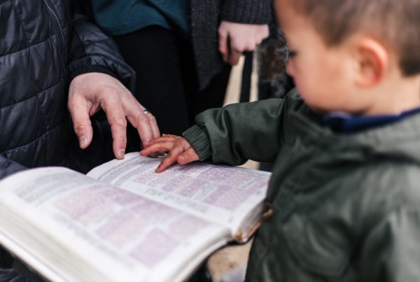 a young boy and his parent trace words on an open Bible