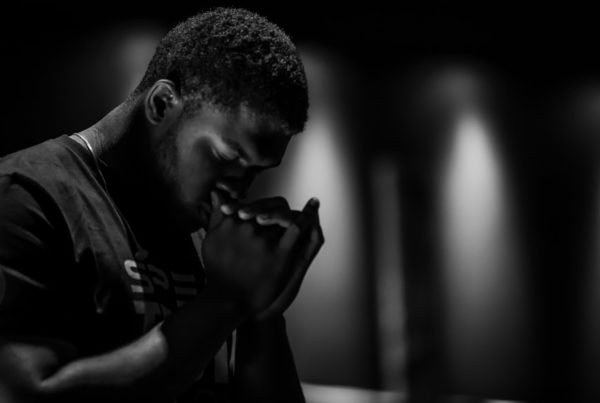 a young black man bows head and folds hands in prayer