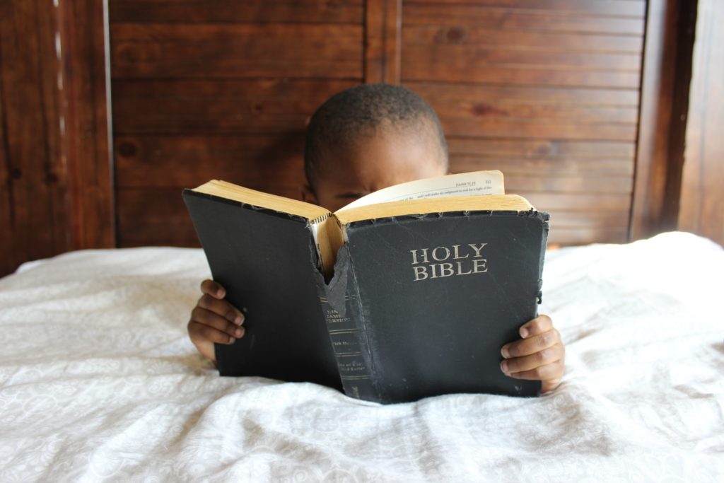 Niño leyendo la Biblia tumbado en la cama