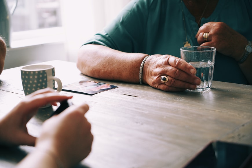 dos pares de manos - jóvenes y mayores - están sobre una mesa con una taza de café y un vaso de agua mientras las dos personas se sientan a hablar
