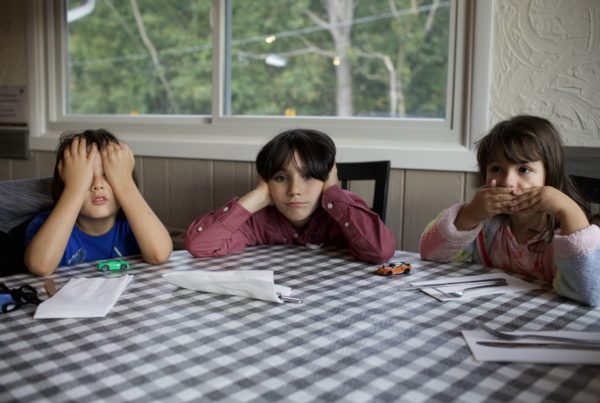 three kids at checkered table cloth do the see no evil, hear no evil, speak no evil hand signs