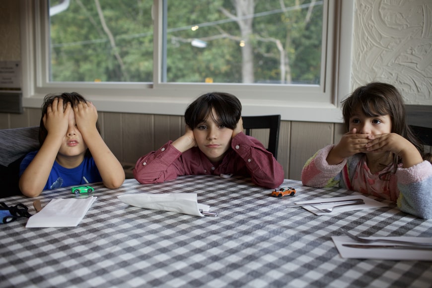 three kids at checkered table cloth do the see no evil, hear no evil, speak no evil hand signs