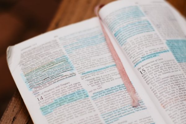 an open Bible with blue highlighting and a red ribbon bookmark