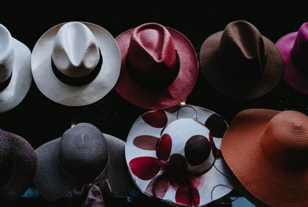 multiple fedoras and wide brimmed colorful hats sit on a table