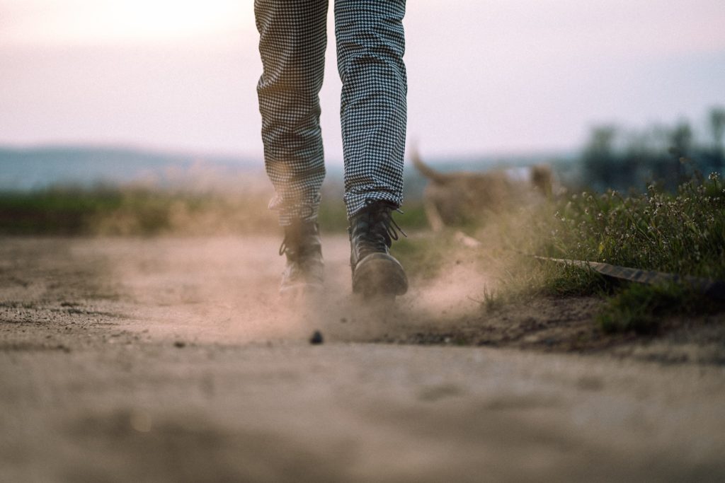 person with black and white checked pants and black boots walks along the dusty ground