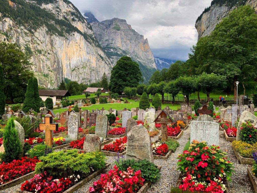 stone grave markers with red flowers and bushes are nestled between mountains in Switzerland