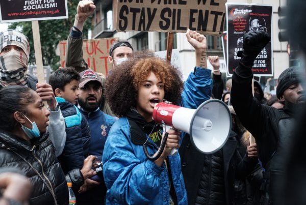 A Black woman in a blue jacket speaks into a megaphone at a racial justice protest