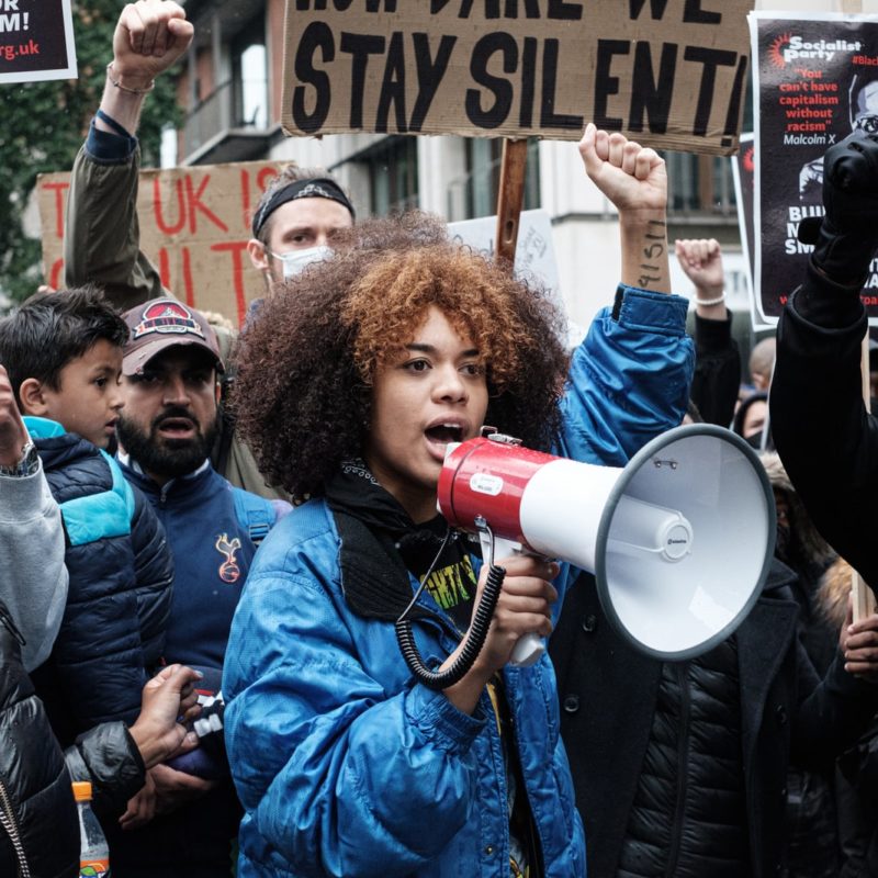 A Black woman in a blue jacket speaks into a megaphone at a racial justice protest