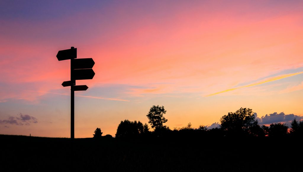 direction sign posts silhouetted by the sunset