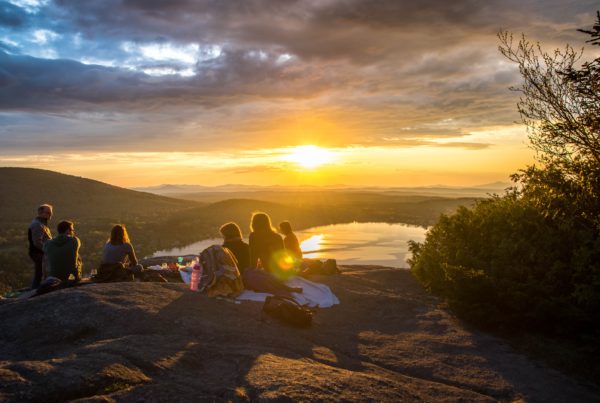 group of people talk on a mountain top with sunset