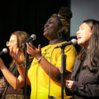 Three young women singing and raising their hands in worship