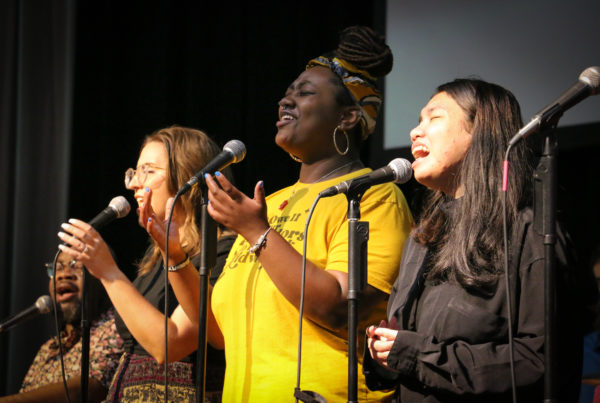 Three young women singing and raising their hands in worship