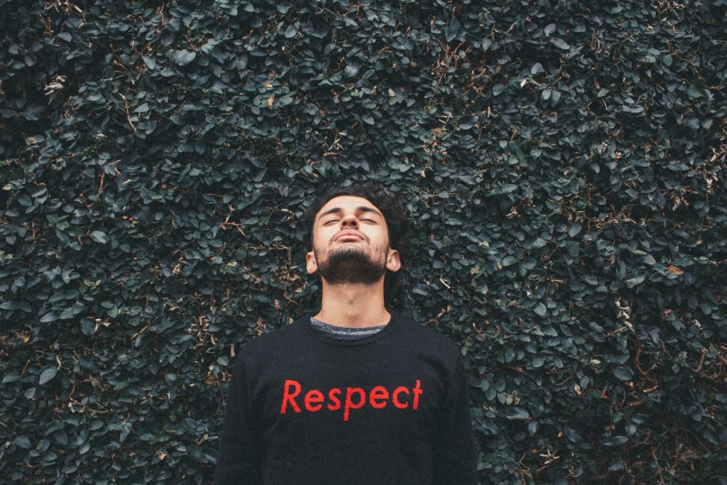 person wearing a shirt that says "respect" standing behind green leafed plants