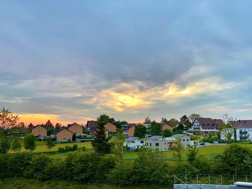 a neighborhood of houses if framed between a cloudy blue-gray sunset and green grass and trees
