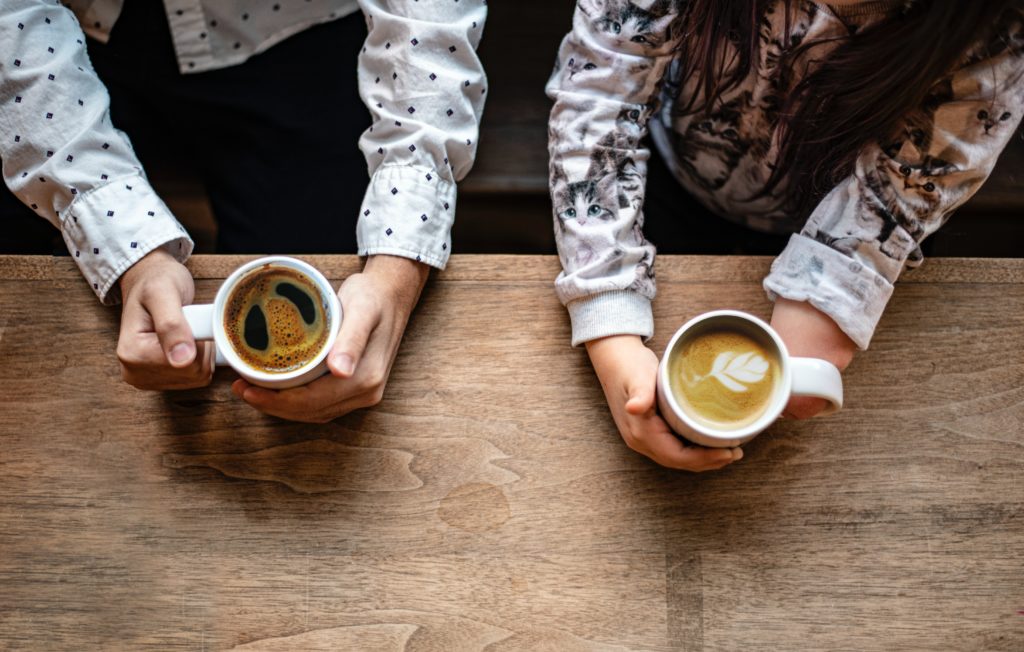 dos personas sostienen tazas de café sobre una mesa de madera, una de ellas con una mano imparcial