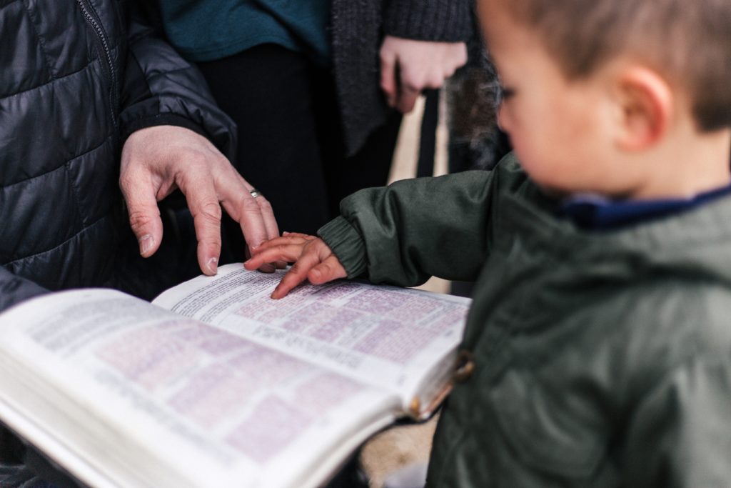 a Bible lays open between an adult and a child, both with a finger touching the page