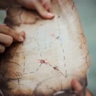 hands hold a worn map with brown and red markings