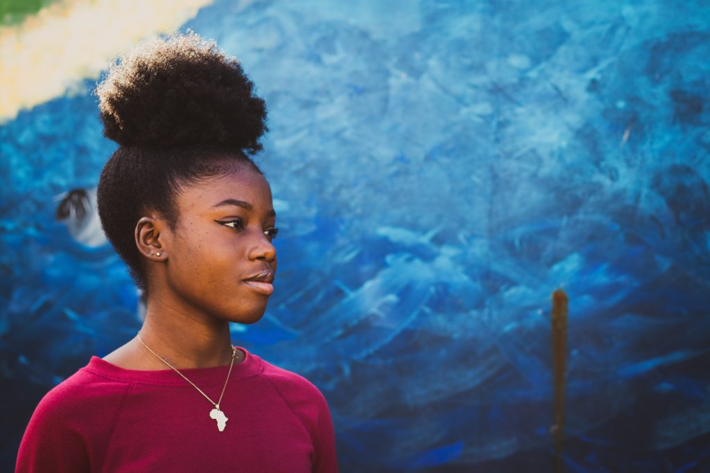una joven negra mira a lo lejos sobre un fondo pintado de azul